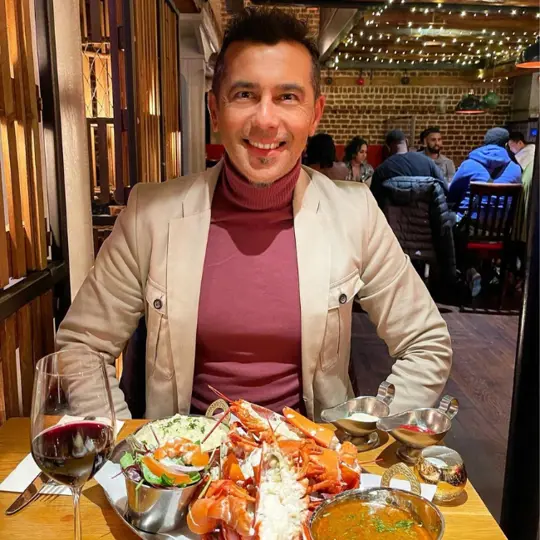 Man smiling with red wine and lobster in front of him from Burger and Lobster